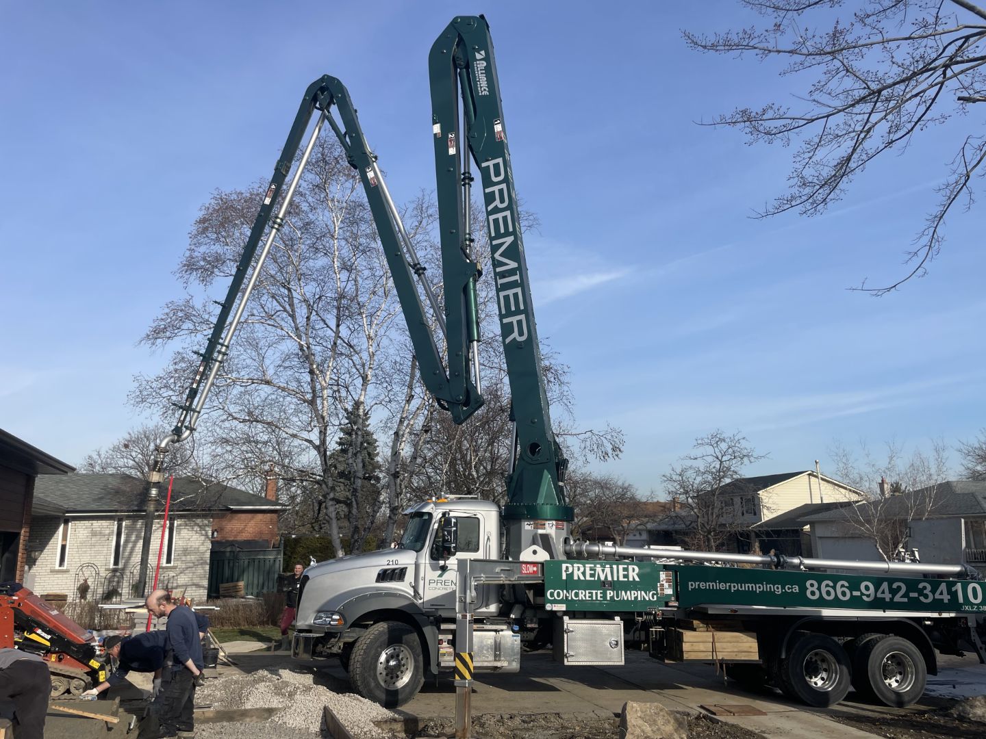 Blog & Market Trends 1 Premier Concrete Pumping 36M boom truck placing concrete for a residential garage slab in a suburban neighborhood with workers preparing the site.