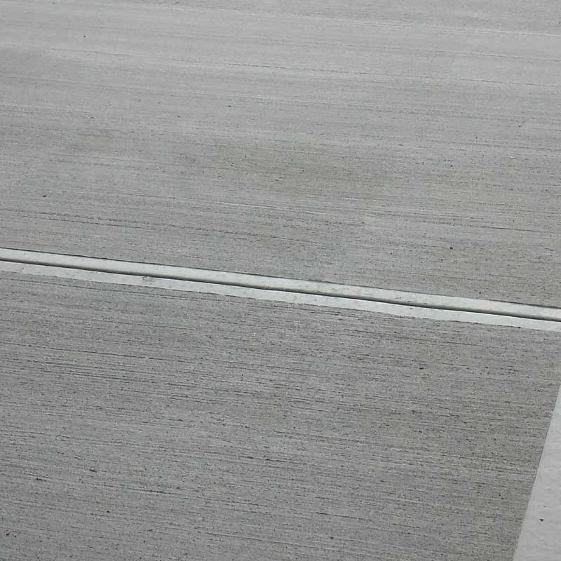 Close-up of concrete with linear broom texture, providing visible traction lines for slip resistance on a flat outdoor surface.