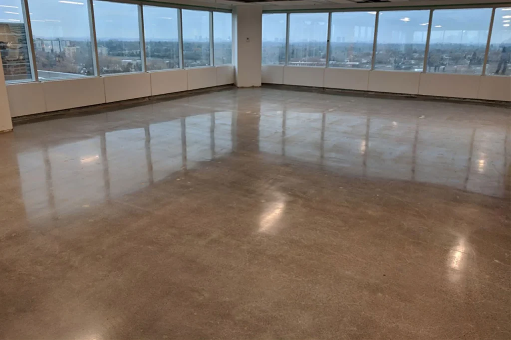 Highly reflective, polished concrete floor inside a commercial high-rise with large windows overlooking a cityscape.